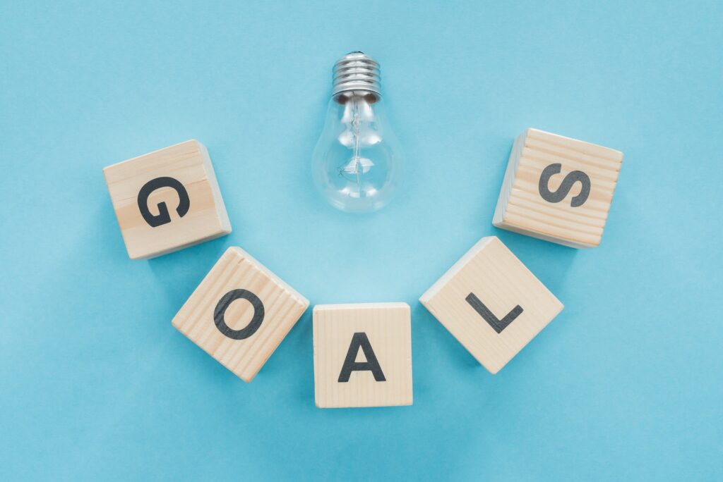top view of light bulb over 'goals' word made of wooden blocks on blue background, goal setting